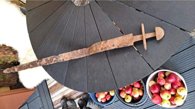 Ett rostigt vikingatida svärd ligger på ett modernt terassbord.
