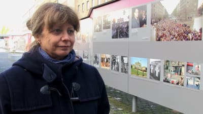 En kvinna till vänster, till höger informativa planscher om Berlinmurens fall.
