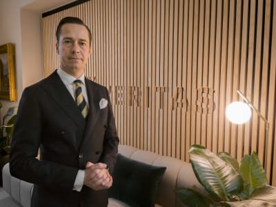 Carl Haglund står i Veritas kontor i Helsingfors iklädd mörk dubbelknäppt kavaj och slips . 