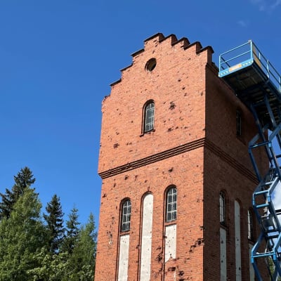Punatiilisen vesitornin kyljessä on sininen saksilava, jolla pääsee vesitornin katon korkeuteen.