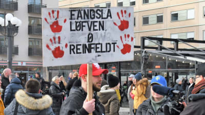 En demonstrant håller en skylt där det står "Fängsla Löfven och Reinfeldt".