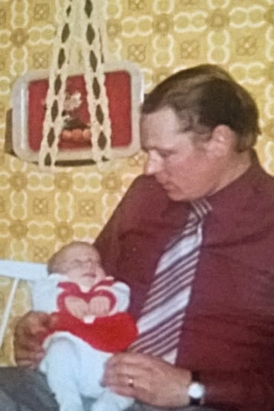 Anna som baby ligger i sin pappas famn.