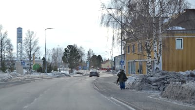 Vöråvägen genom centrala Vörå, fotot taget under en vinterdag i slutet av februari. Vägen är bar men längs sidorna finns snödrivor. En person går på trottoaren. Längre fram syns en bil på vägen.