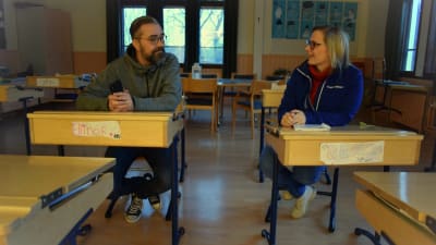 Sabina Simola-Ström och Micke Gunnarsson sitter i var sin pulpet i ett klassrum och pratar med varandra.