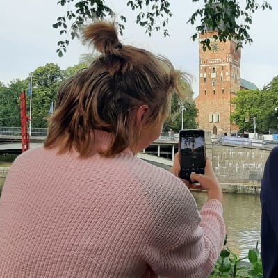 Två personer sitter med ryggen mot kameran och tar med telefonen ett foto av Åbo domkyrka.