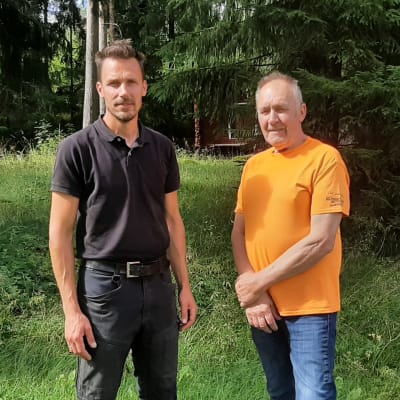 En man i svart och en i oranget står bredvid varandra och ler mot kameran.