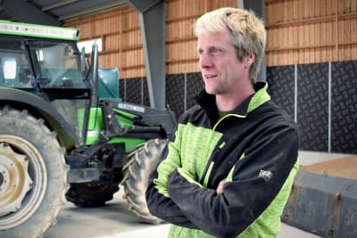 Claus Blomberg står i en lagerhall framför en grön traktor.