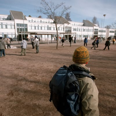 En pojke står ensam på skolgården och tittar på när andra barn leker.