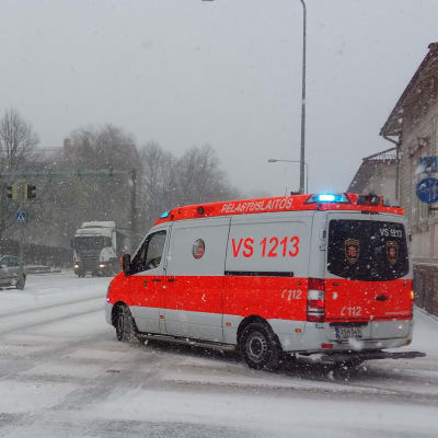 En ambulans på utryckning svänger runt ett gathörn på snöiga gator.