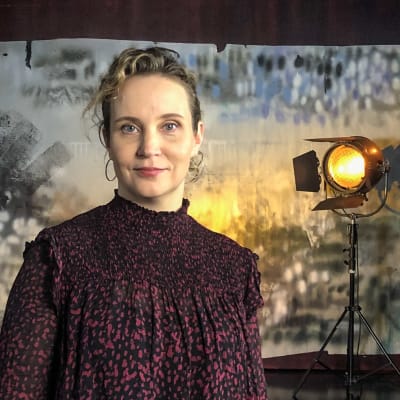 Porträttbild av Kirsikka Saari som står i en studio med stuidolampor i bakgrunden. 
