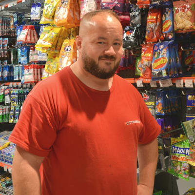 En man i röd skjorta står framför en butikshylla med godis.
