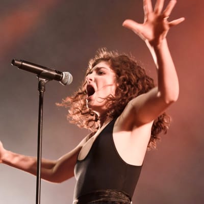 Lorde har armarna utsträckta och sjunger i en mikrofon som är i en mikrofonställning.