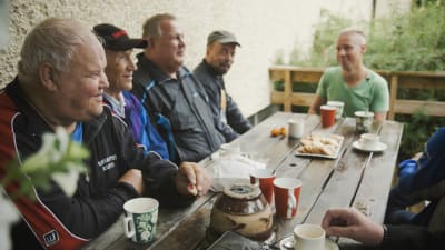 Grupp med män dricker kaffe vid ett terassbord.