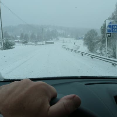 Hand som håller i bilens ratt, snöig väg.