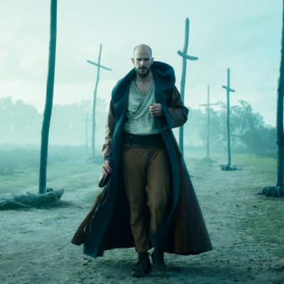 Svenska skådespelaren Gustaf Skarsgård spelar trollkarlen Merlin i tv-serien Merlin. Här ser man honom gå i ett disigt mörkt landskap där flera träkors syns.