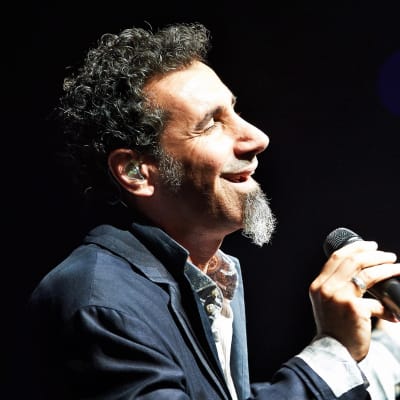 Serj Tankian sjunger i en mikrofon som han håller i handen.