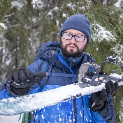 Aarne Granlund puhdistaa liukulumikenkää lumesta metsässä.