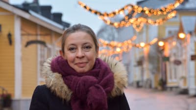 Ann-Sofie Silvennoinen står vid en gata i Gamla stan i Borgå. I bakrunden syns gamla trähus och julbelysning. 