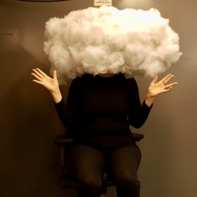 Mustiin pukeutunut nainen istuu iso pilvi päässä ja kädet levällään.