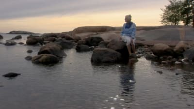 Irmelin Sandman Lilius sitter på en sten i havet.