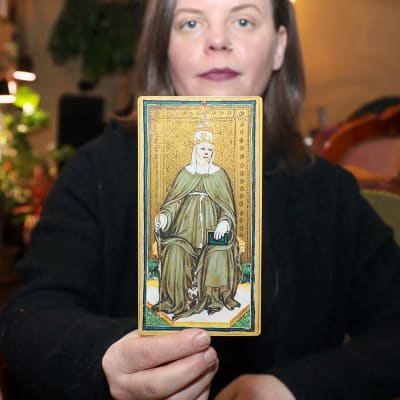 Tarotpuodin luova johtaja Mikaela Holmberg esittää kameralle italialaista, käsinmaalattua ylipapitarta esittävää tarotkorttia.