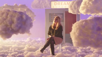 Toimittaja, esseisti Anu Silfverberg istuu pilvien päällä jakkaralla studioon lavastetussa taivaassa, taustalla näkyy Dream Automat -kuvauskoppi.