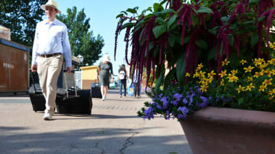 En man i sommarkläder drar en kappsäck bakom sig längs med aura Å. Blommor i en kruka i förgrunden.
