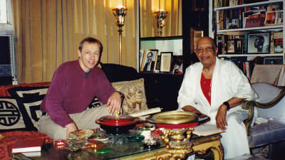 Wade Mikkola ja Donald Shirley istuvat sohvapöydän ääressä lukuisten koriste-esineiden ja valokuvien ympäröiminä.