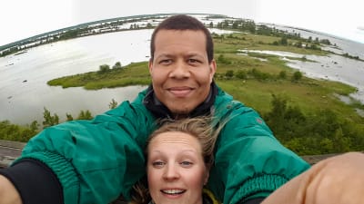 Ari tar en selfie med sin sambo högt uppifrån. I bakgrunden syns sjöar och gröna ängar.