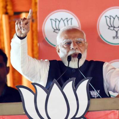 Narendra Modi hytter med pekfingret vid ett podium klätt i partiets logga.