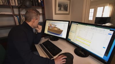 En man sitter vid en dator och på skärmen finns en 3d ritning av en båt. 