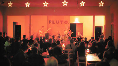 After Eightin järjestämä Pluto-festivaali. Ihmisiä istuu hämärässä kahvilassa kuuntelemassa Crash-yhtyettä vuonna 1998.