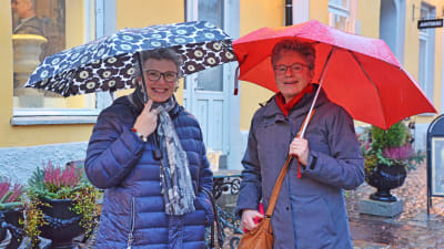 Två damer står bredvid varandra under sina paraplyer och ler.