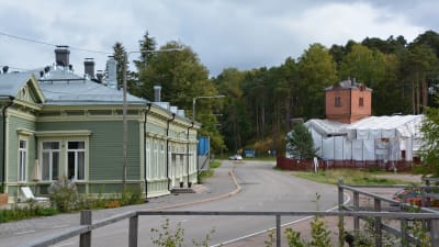Till vänster syns ett stort grönt hus, den gamla järnvägsstationen. På andra sidan vägen, till höger, finns ett tegelhus med ett torn. Taket är intäckt med vita presenningar.