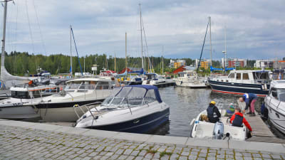 På bilden syns flera rader med segelbåtar och motorbåtar i Borgå å. Längst nere till höger i bilden finns en öppen motorbåt med några personer i. En man håller på att förtöja båten.