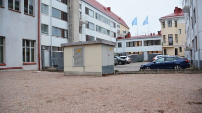 En transformator på en sandplan inne på en gårdsplan. I bakgrunden syns höghus.