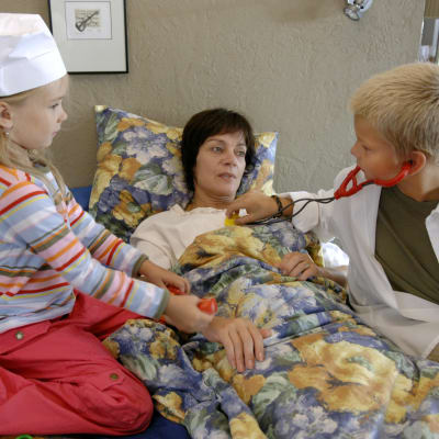 Kotikadun Eeva (Lena Meriläinen) makaa sängyssä. Häntä hoitavat lääkärileikissä Kerttu (Linda Liikka) ja Jarkko (Santeri Nuutinen).