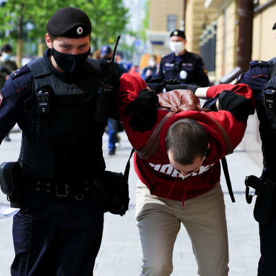 En man grips av polis. Han står mellan två poliser, nerböjd medan de håller ner honom.
