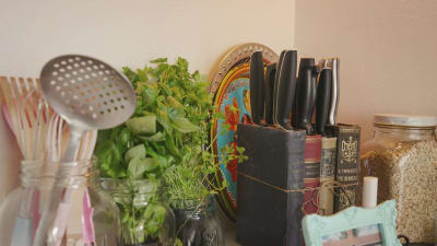 Pöydällä leikkuuveitsiä vanhoista kirjoista tehdyssä veitsitelineessä, muita keittiövälineitä ja yrttejä ruukuissa.