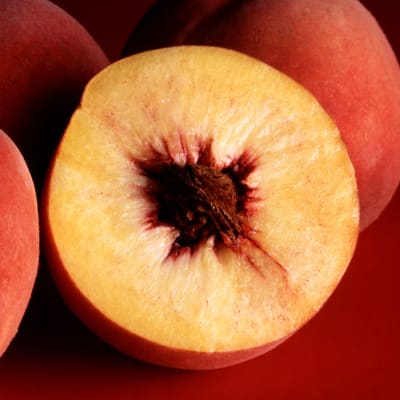 En persika skuren på hälft. I mitten av persikan sitter dess kärna.