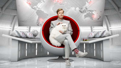 Johan Glans sitter i en rund fotölj likt en skurk från en james bond film. han har en vit angorakatt i famnen.