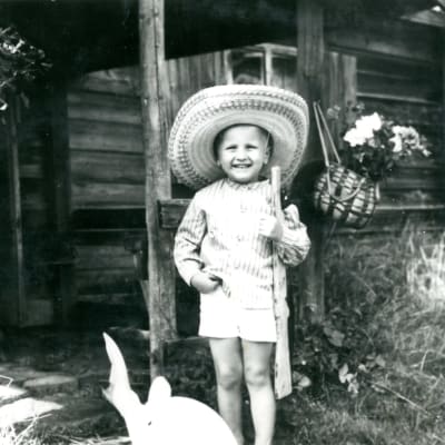 Jaakko Heinimäki pikkupoikana mustavalkoisessa valokuvassa puinen pyssy olalla ja valtava sombrero päässään.
