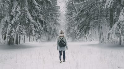 Tyttö kävelee metsätiellä johon on satanut ensilumi. 