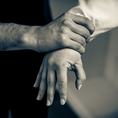 Miehen käsi puristaa naisen kättä.