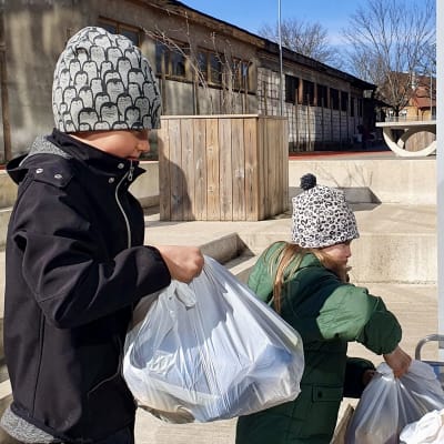 Två barn tar emot veckans skollunchpåse som delas ut i deras skola i Tallinn under coronapandemin.
