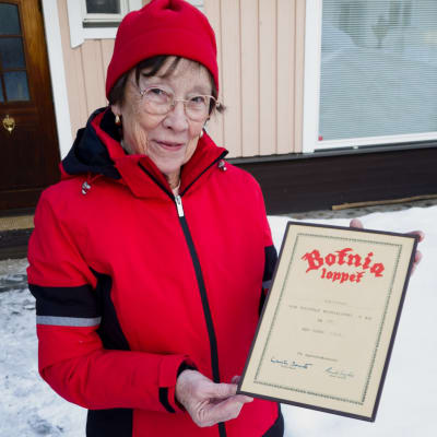 En kvinna i röd vinterjacka håller i ett diplom