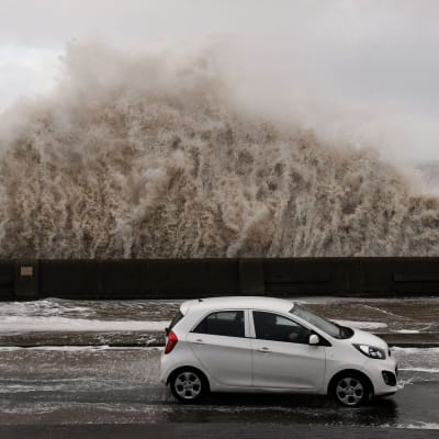 Stormen Eleanor slår upp en våg över en bil i Storbritannien.