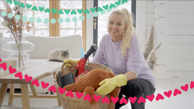 Kuvassa siivousvaikuttaja Sonia Lindholm on kyykyssä ja pitelee käsissään pehmoleluilla ja muilla kodin tavaroilla täytettyä isoa koria.