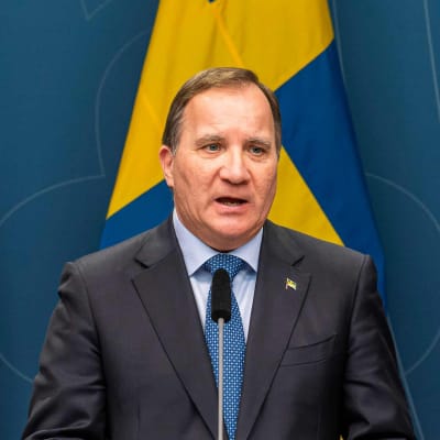 Sveriges statsminister Stefan Löfven talar i en mikrofon. Bakom honom syns Sveriges flagga.