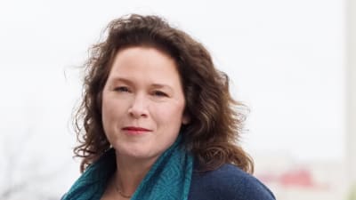 En kvinna (Pella Thiel( i blå tröja och blå scarf och långt brunt hår.